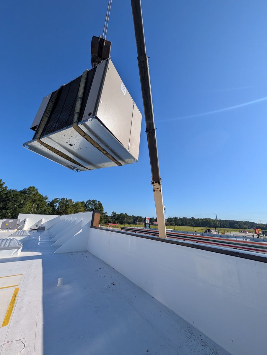 Crane lifting an HVAC unit to a commercial rooftop